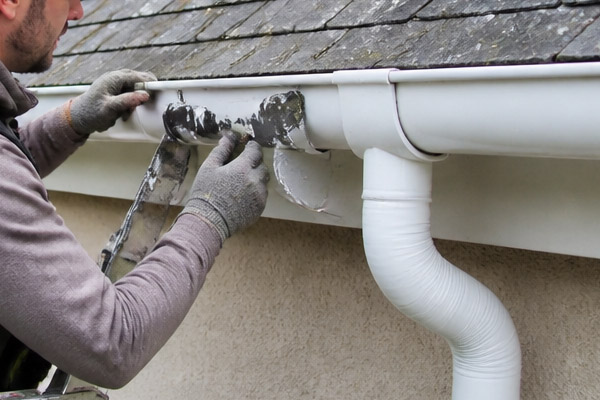 Artisan zingueur réparant un raccord d'étanchéité défectueux sur une gouttière en PVC blanc